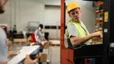 A man on the left holds a clipboard and a man on the right is turned while sitting on a piece of equipment.